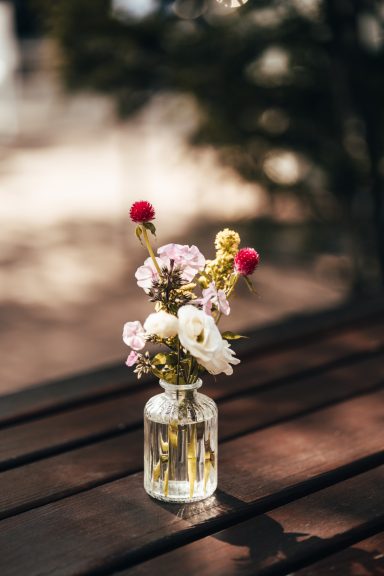 Ein Blumenstrauß mit bunten Blüten in einer Glasvase auf einem Holztisch.